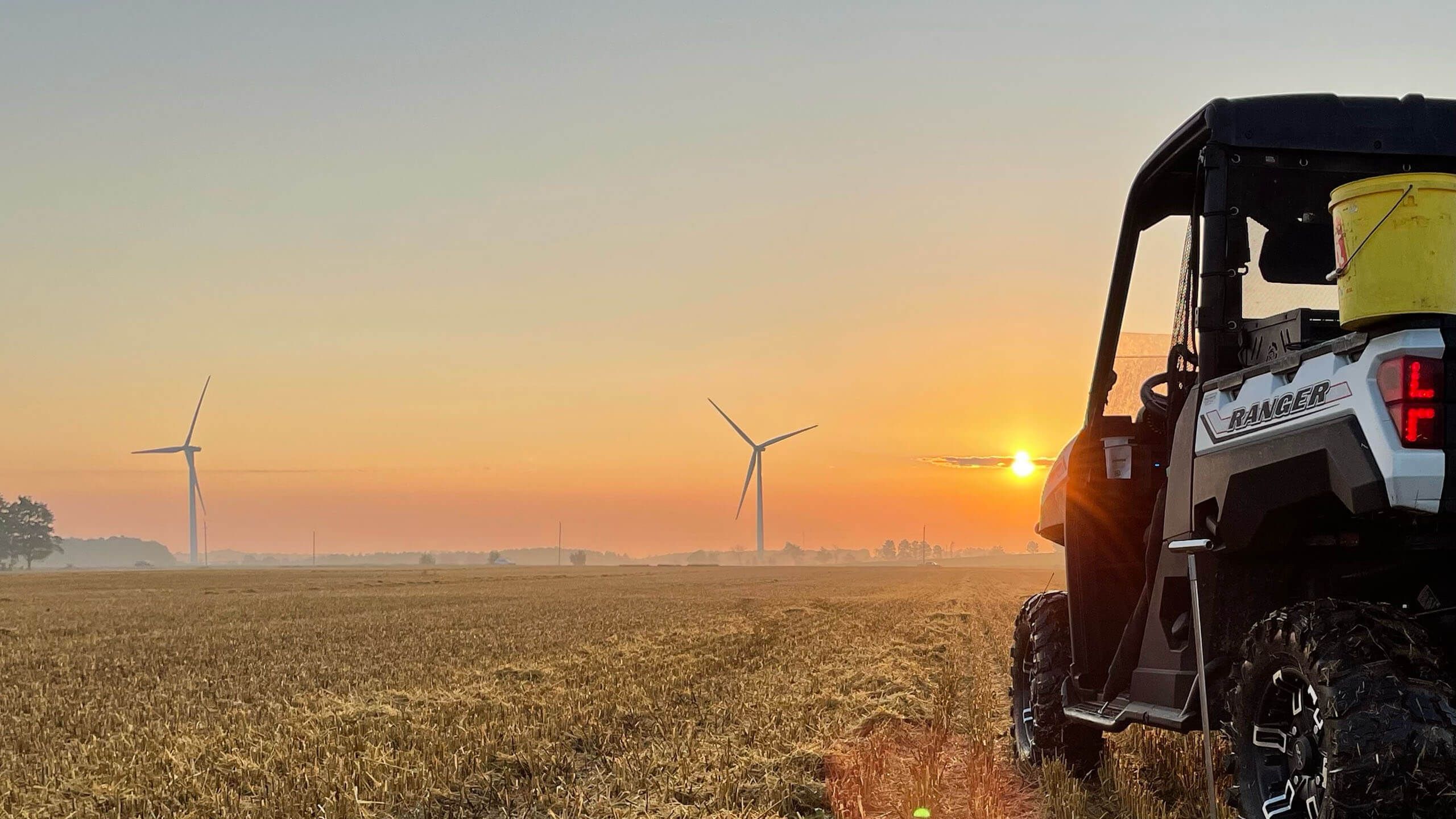 Holmes Agro Ranger on crop with windmills and sunset in the background